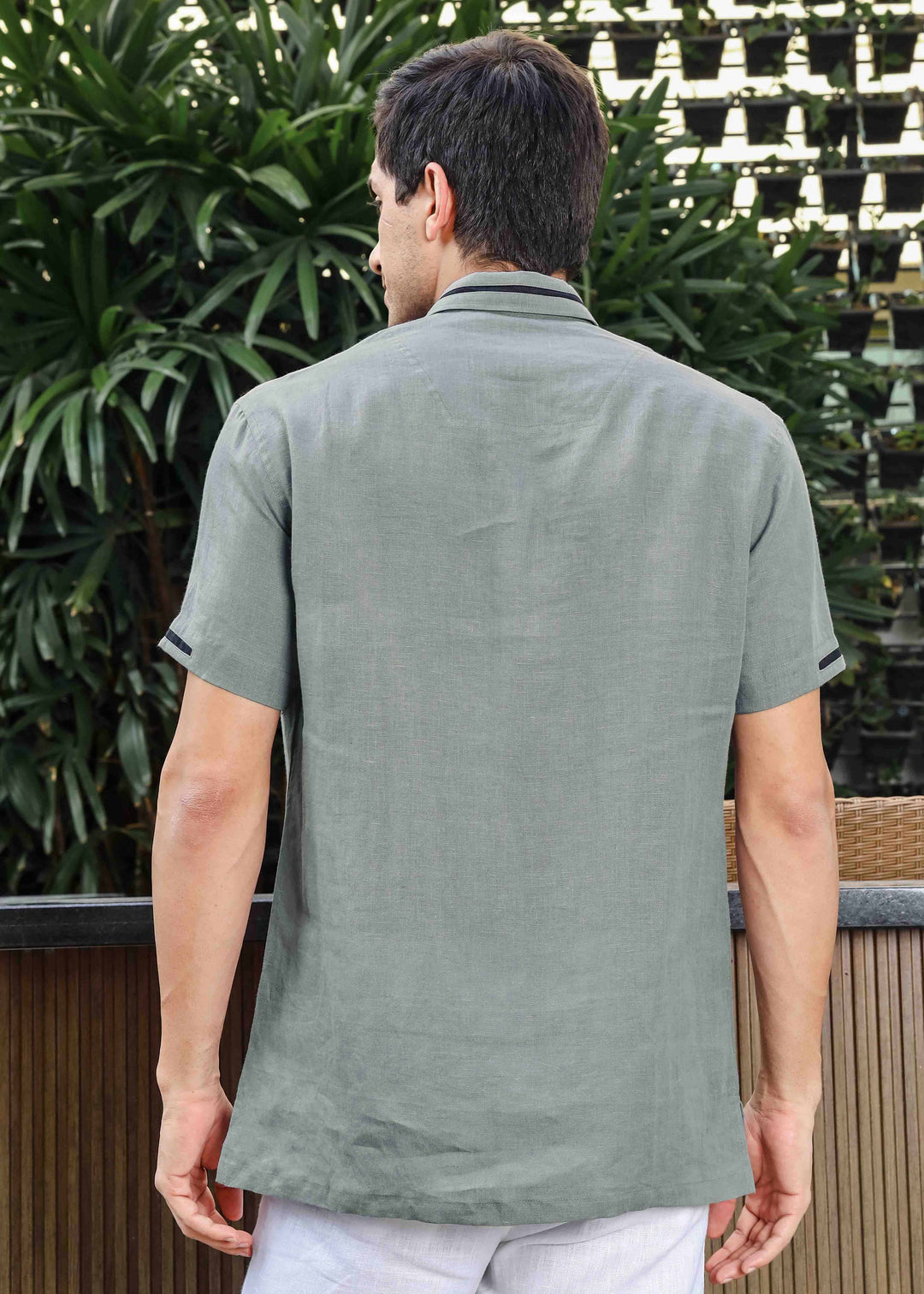 Man wearing a 100% pure linen grey t-shirt standing outdoors with plants in the background