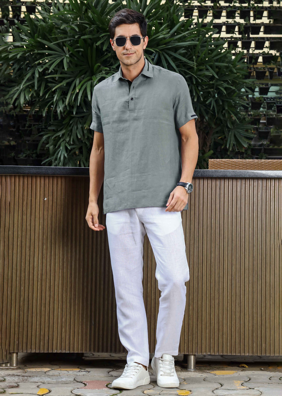 Man wearing a 100% pure linen grey t-shirt and white pants standing outdoors with plants in the background