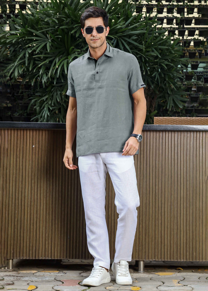 Man wearing a 100% pure linen grey t-shirt and white pants standing outdoors with plants in the background