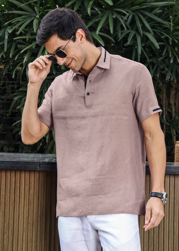Man wearing a 100% pure linen cameo pink t-shirt and white pants standing outdoors with greenery in the background