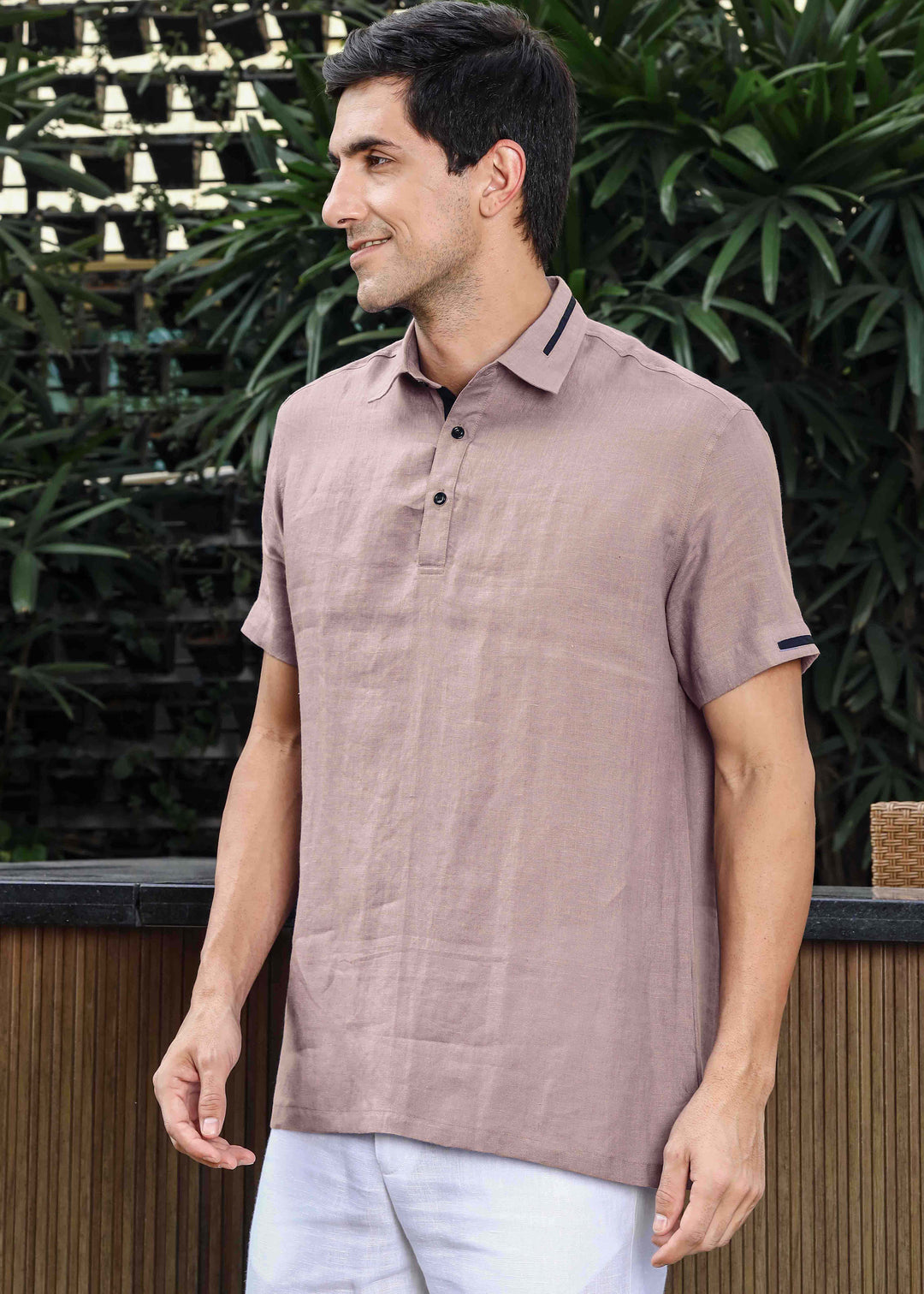 Man wearing a 100% pure linen cameo pink t-shirt standing outdoors with greenery in the background