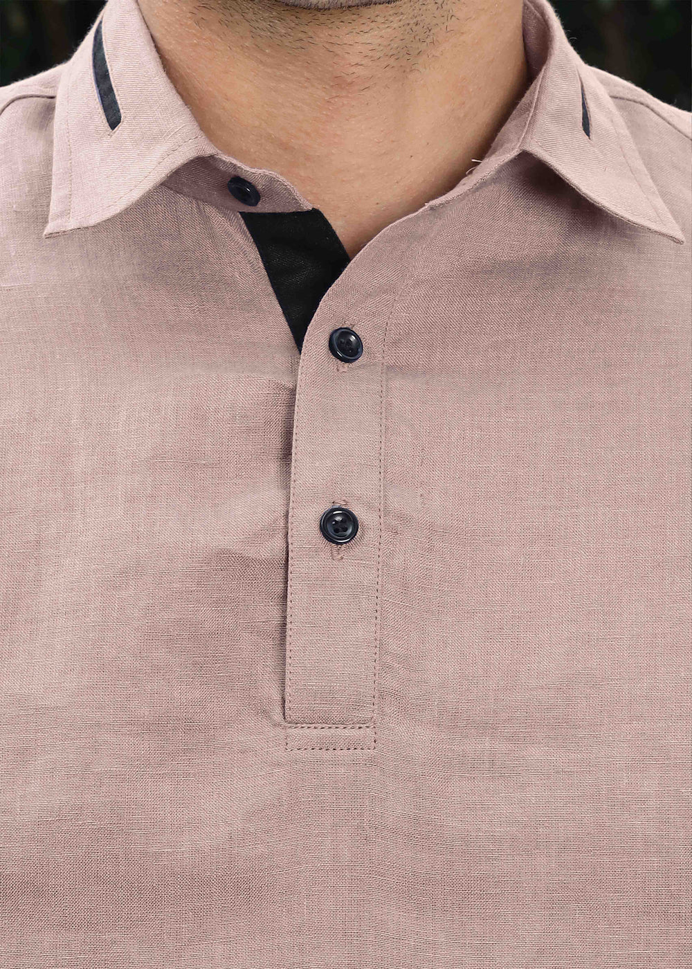 Close-up of a 100% pure linen cameo pink t-shirt with black buttons and trim on a blurred background