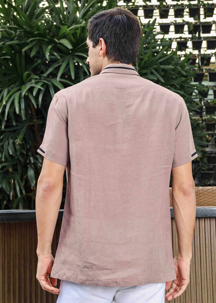 Man wearing a 100% pure linen cameo pink t-shirt with a collar, standing outdoors with greenery in the background.