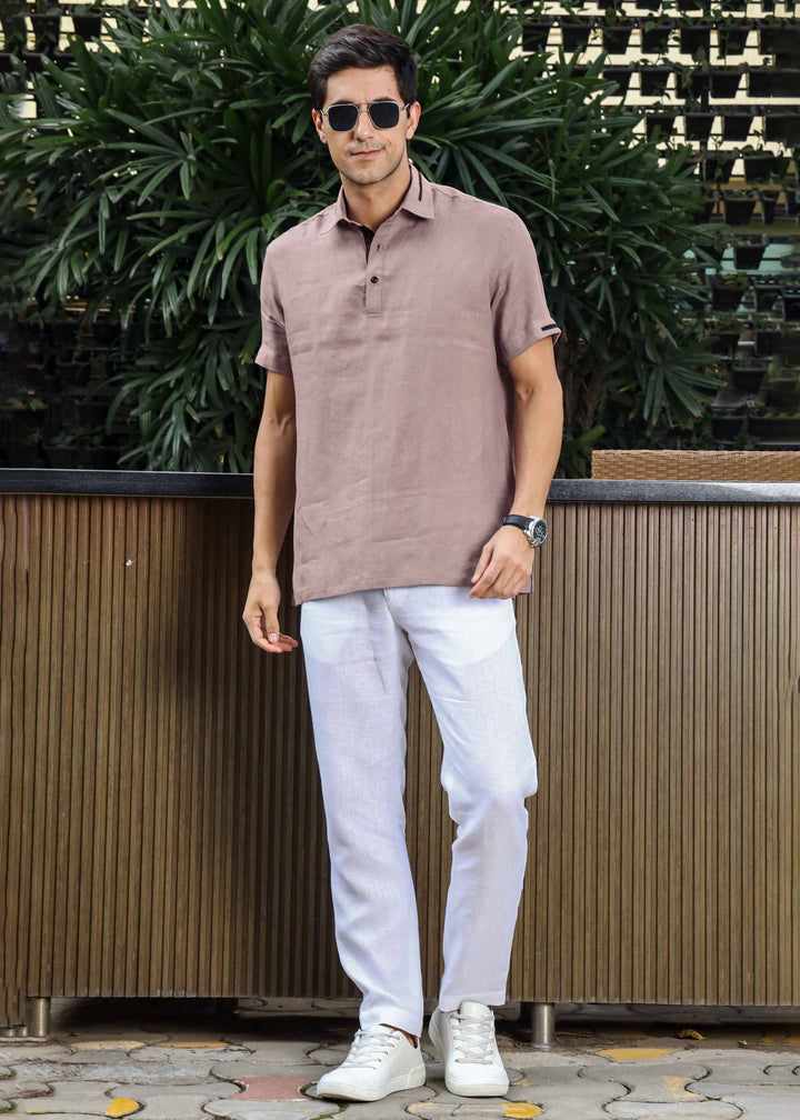 Man wearing a 100% pure linen cameo pink t-shirt and white pants standing outdoors with greenery in the background