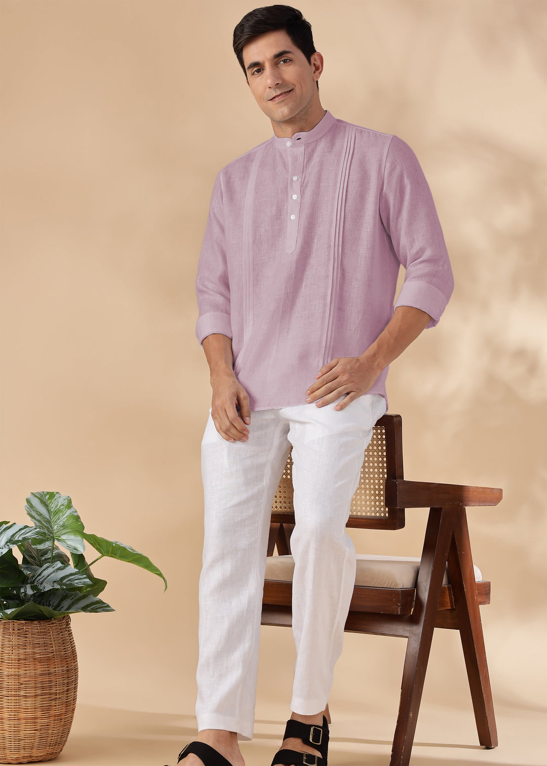 Man wearing a 100% pure linen cameo pink short kurta and white pants sitting on a wooden chair with a beige background