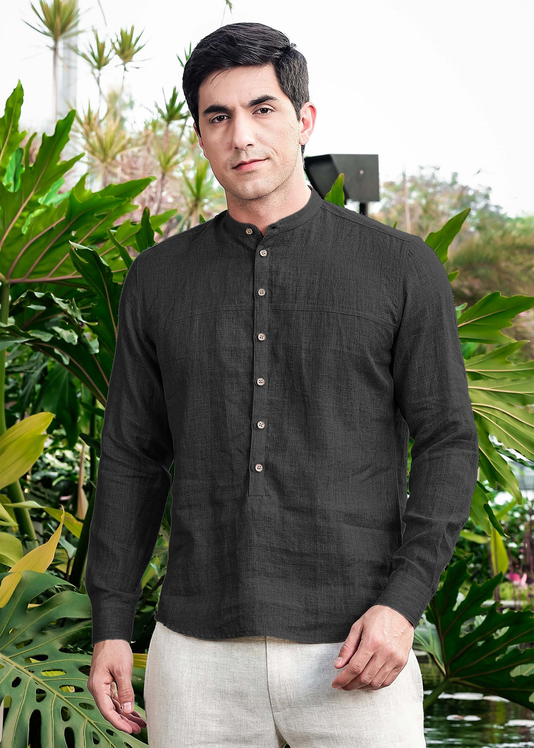 Man wearing a 100% pure linen black short kurta with buttons in front of green foliage