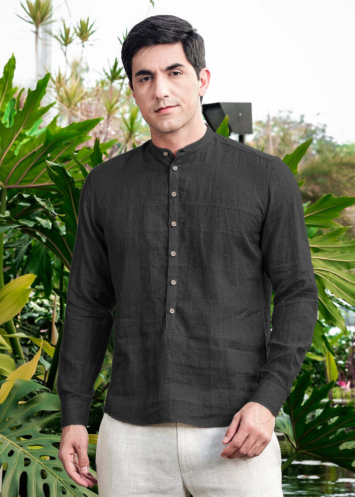 Man wearing a 100% pure linen black short kurta with buttons in front of green foliage