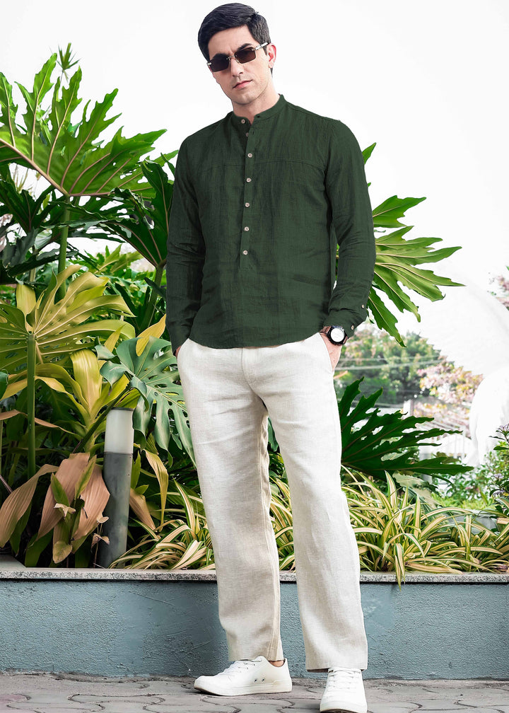 Man wearing a 100% pure linen dark fern green short kurta and white pants standing in front of green plants
