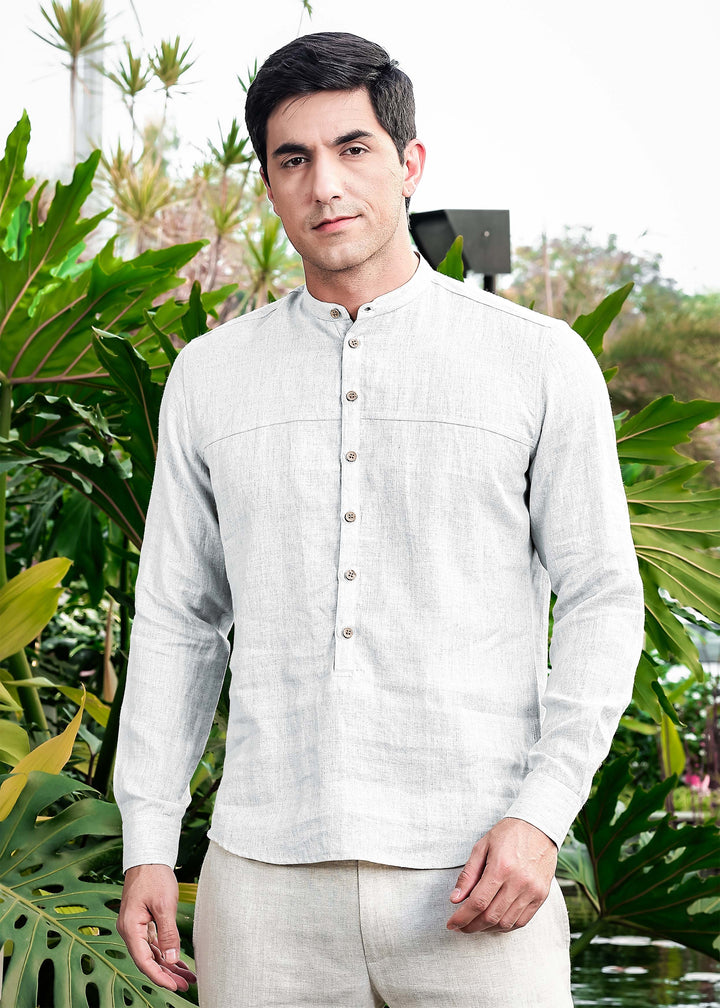 Man wearing a 100% pure linen white short kurta and pants standing in front of green foliage