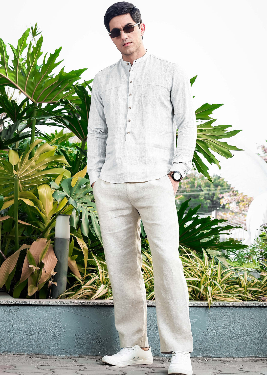 Man in a 100% pure linen white short kurta and ecru pants standing in front of green plants