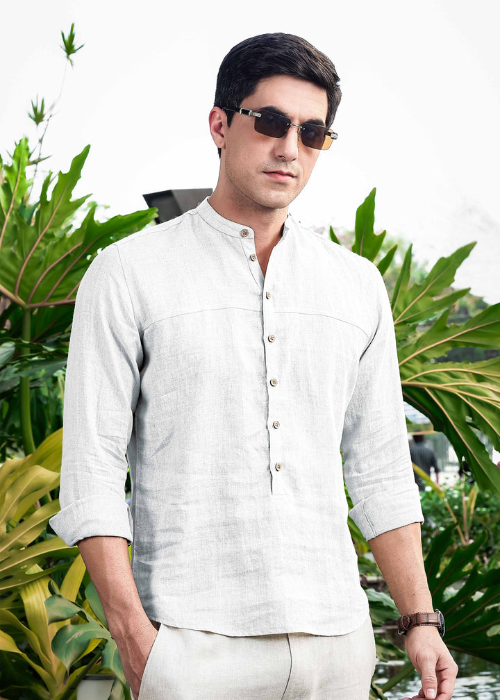 Man wearing a 100% pure linen white short kurta and sunglasses standing in front of green foliage