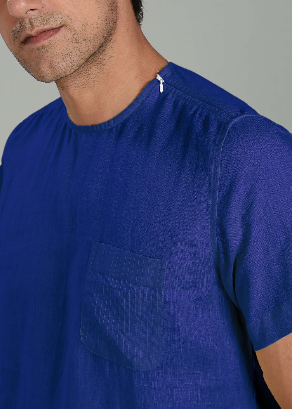 Close-up of a person wearing a 100% pure linen egyptian blue t-shirt with a pocket on a gray background