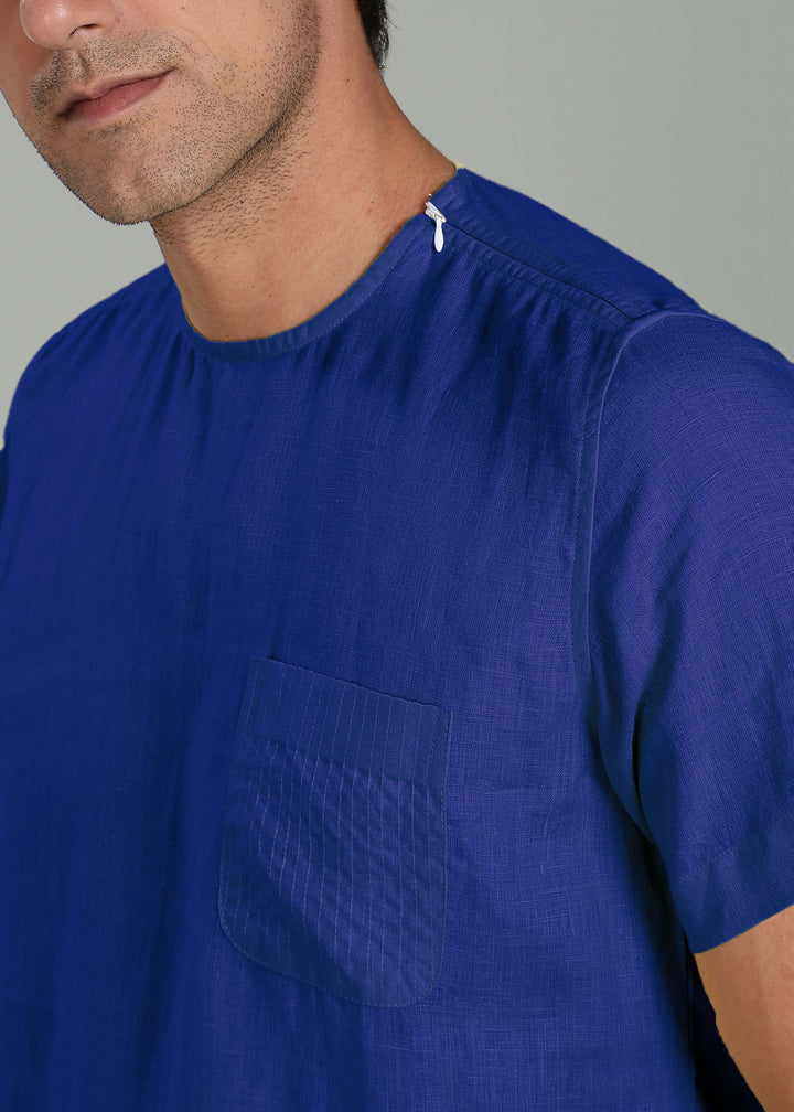 Close-up of a person wearing a 100% pure linen egyptian blue t-shirt with a pocket on a gray background