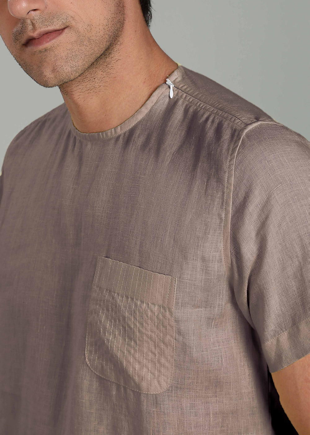 Close-up of a man wearing a 100% pure linen fawn pink t-shirt with a pocket on a plain background