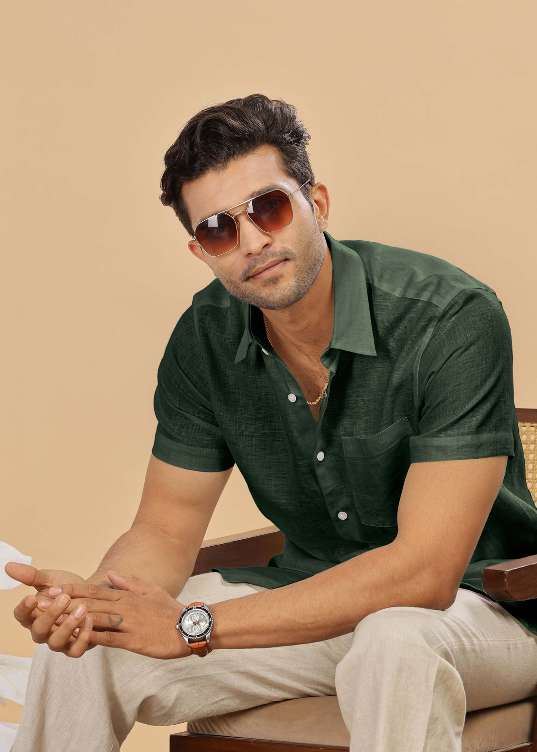 Man wearing sunglasses and a 100% pure linen dark fern green shirt sitting on a chair with a beige background
